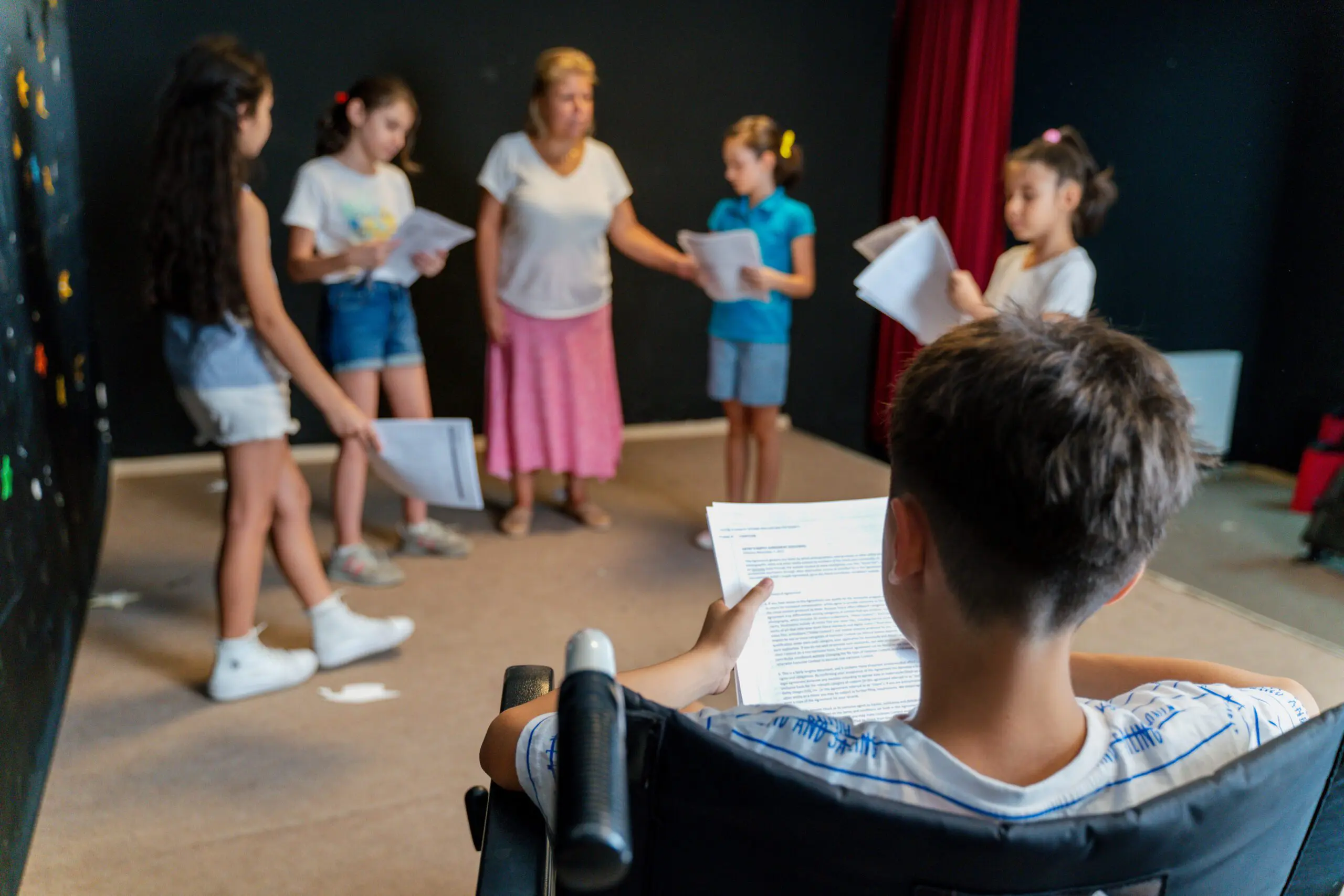 Children with scripts in their hands, rehearsing at drama club with a teacher.