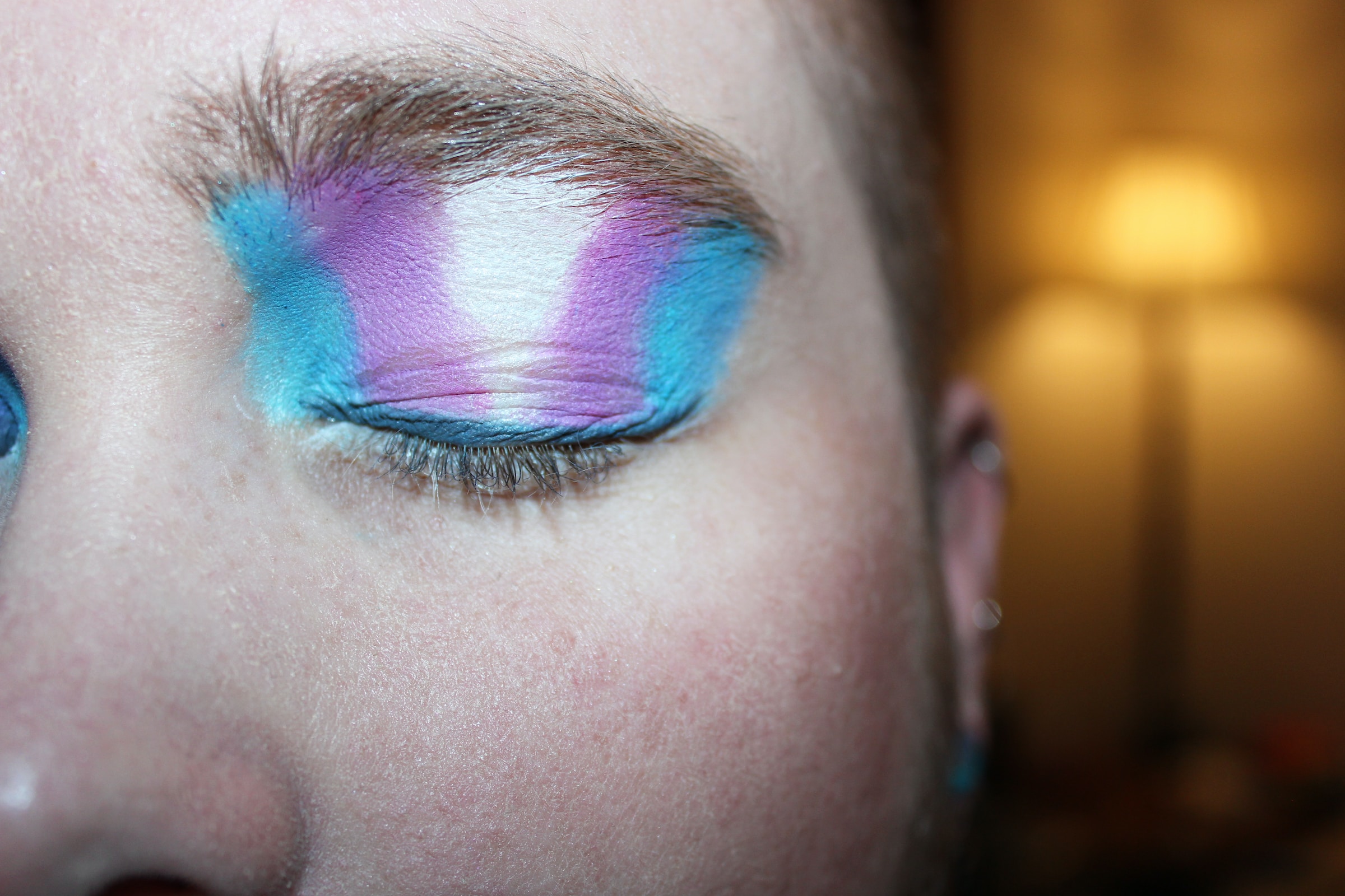 Closed eye with trans pride flag coloured make up on it