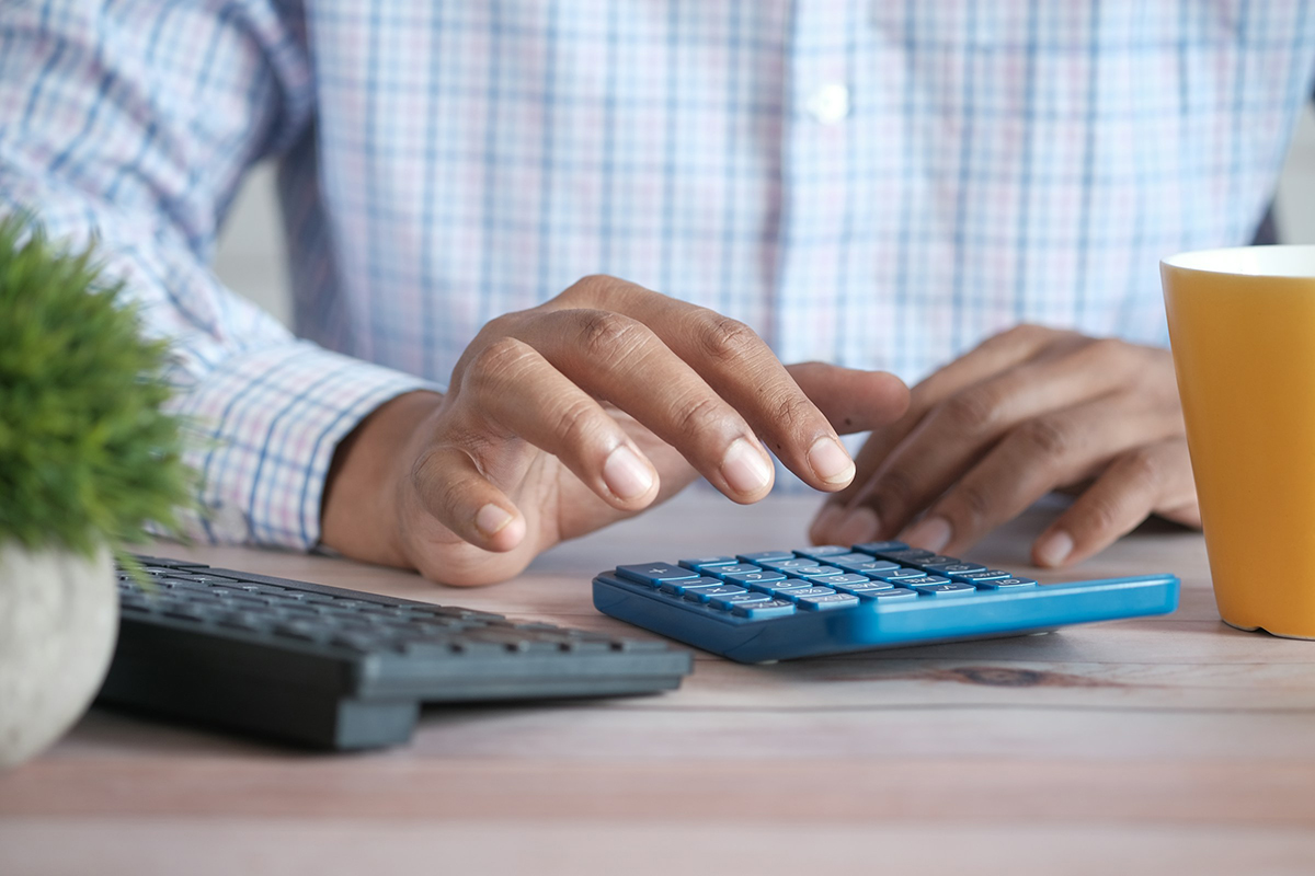 A hand preparing to type on a calculator next to a computer keyboard