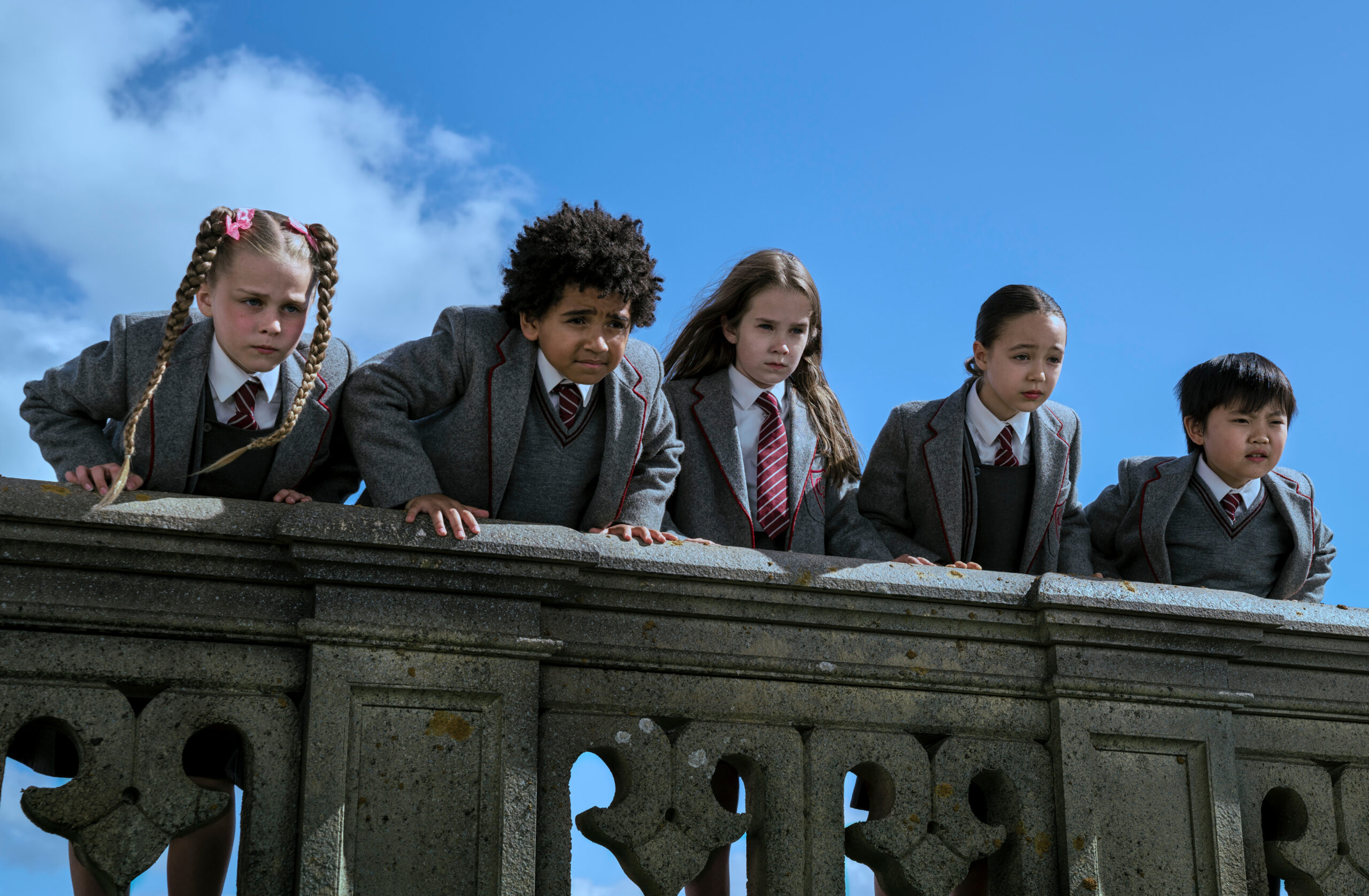 Matilda and her classmates peering over a stone fence in 'Matilda the Musical' film