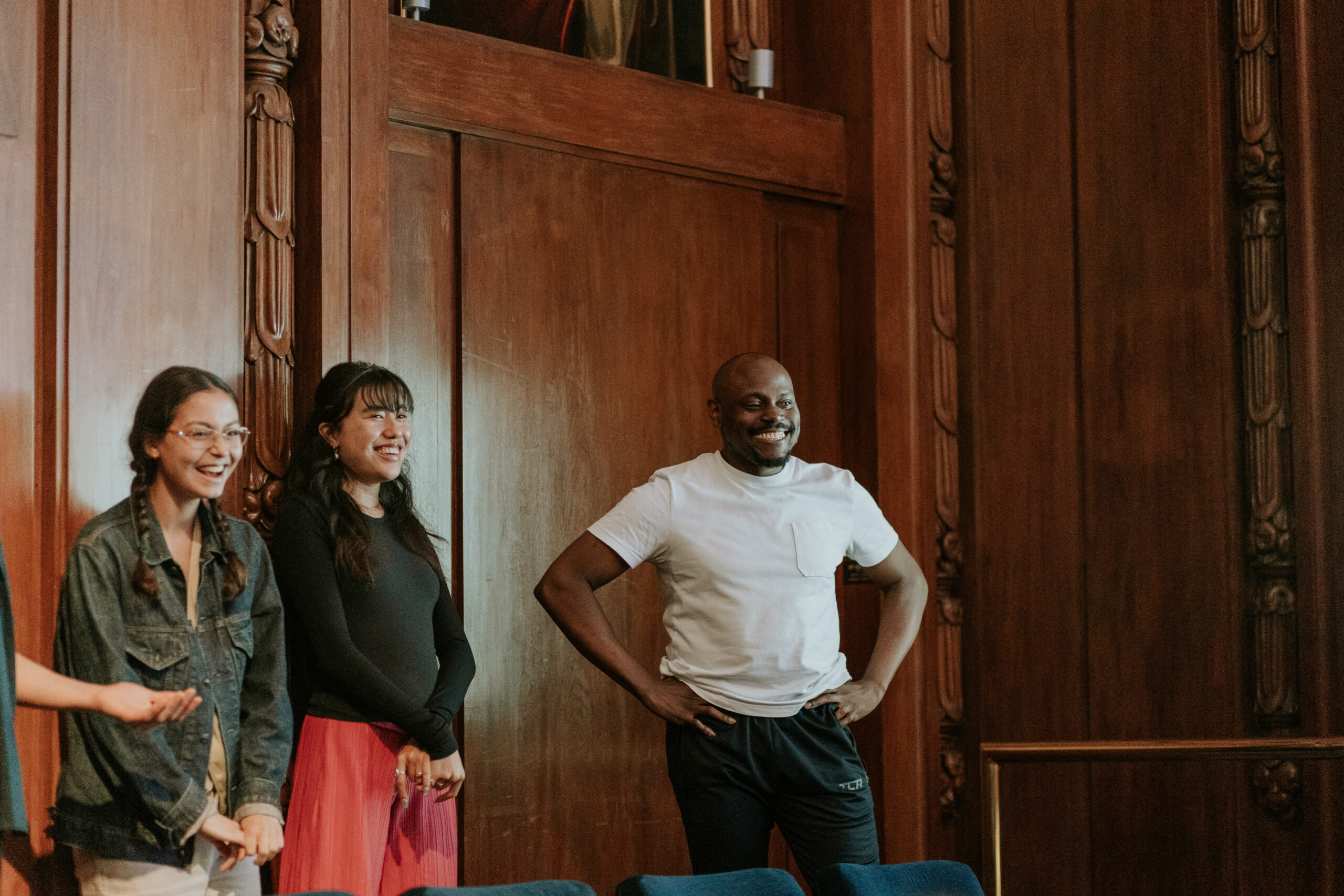 An actor and two actresses smiling at the back of a wooden room while they wait to perform.