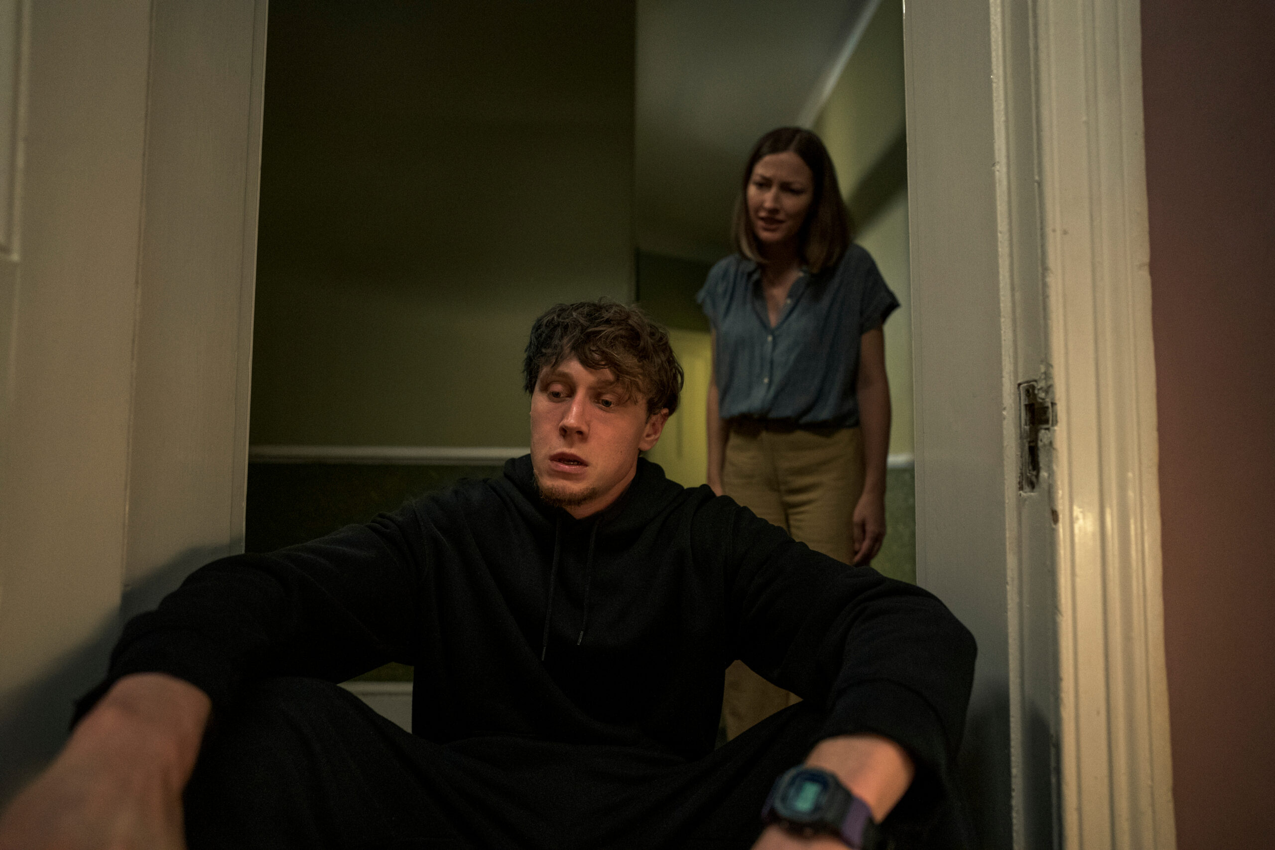 Actor George MacKay as 'Toby' in 'I Came By' sitting in a doorway with 'Lizzie' standing behind him