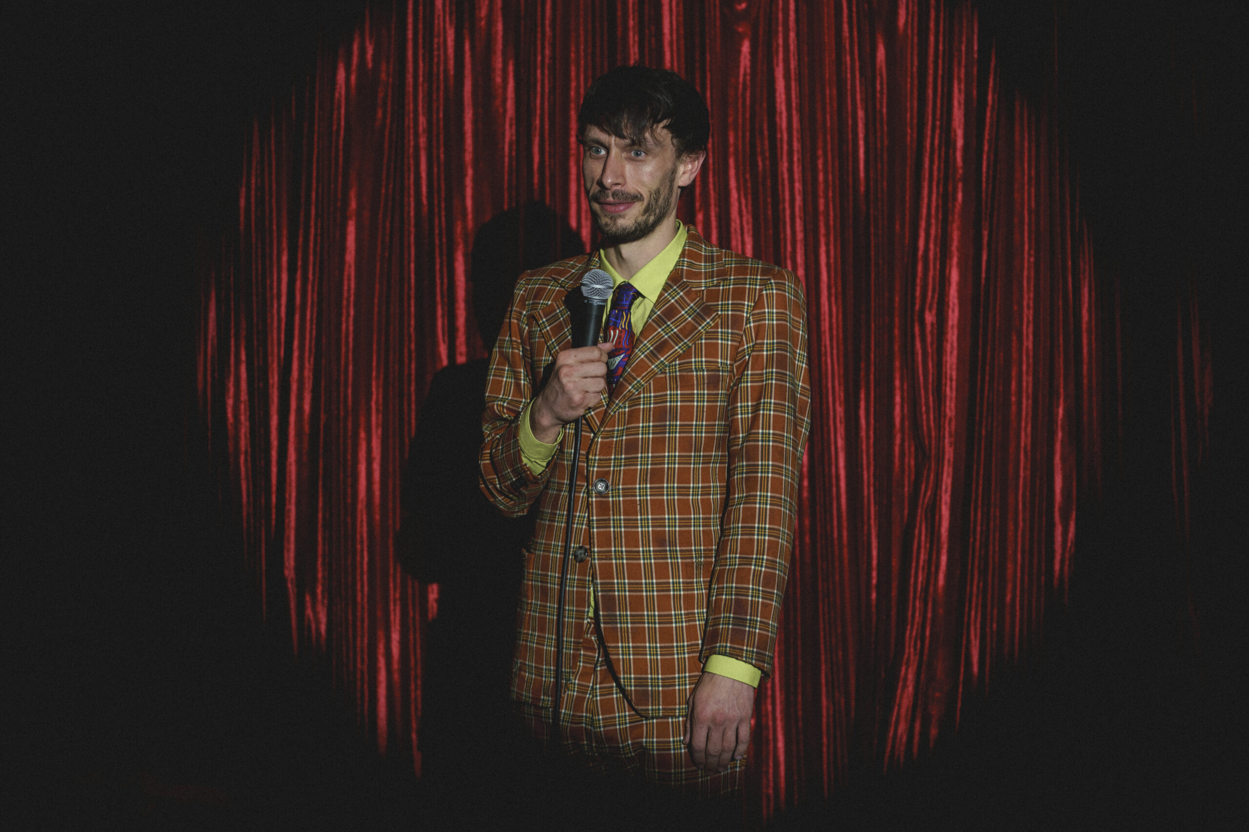 Richard Gadd holding a mic in front of red curtains in 'Baby Reindeer'