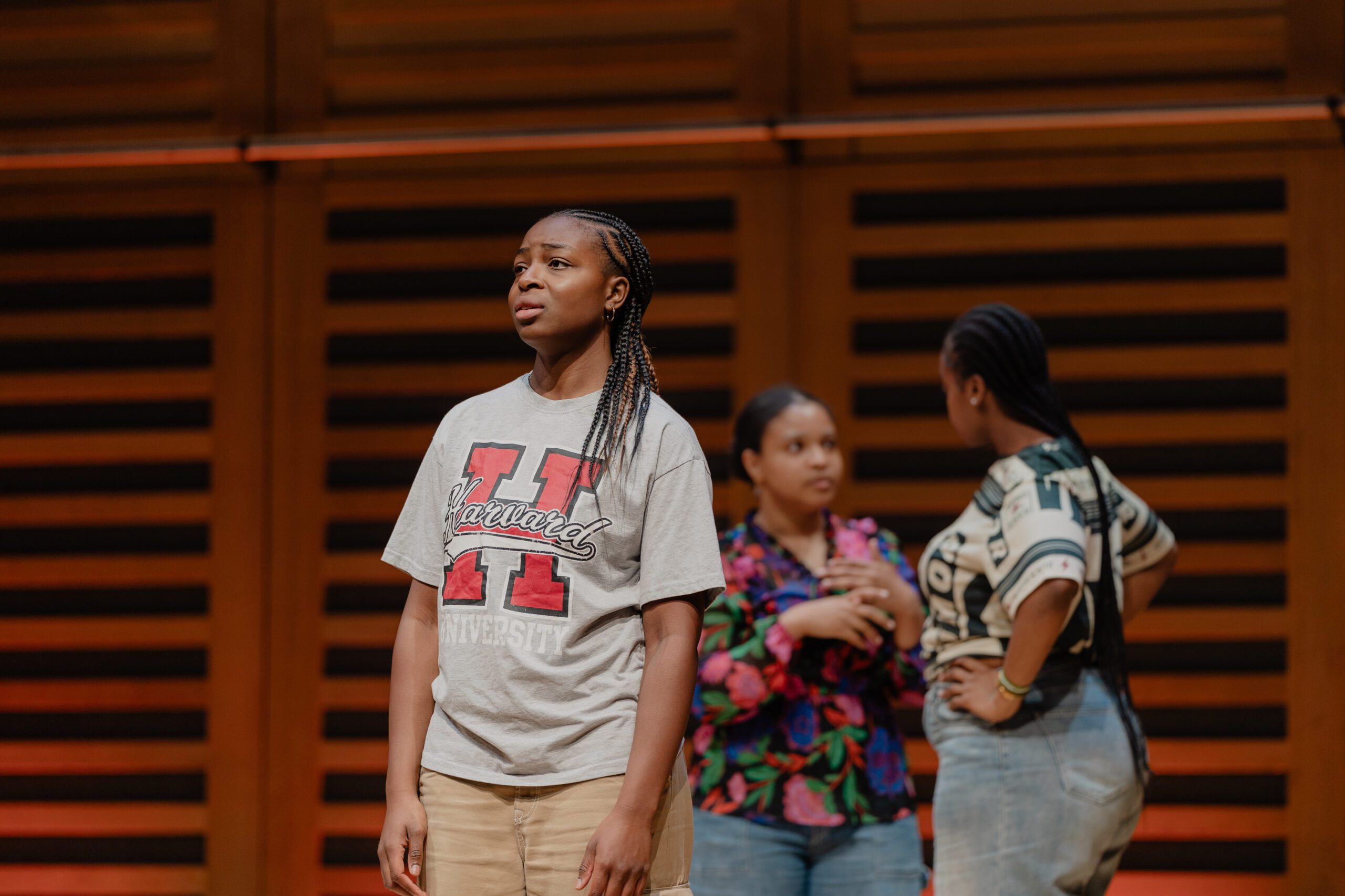 An actress looking concerned on stage while two other actresses chat behind her