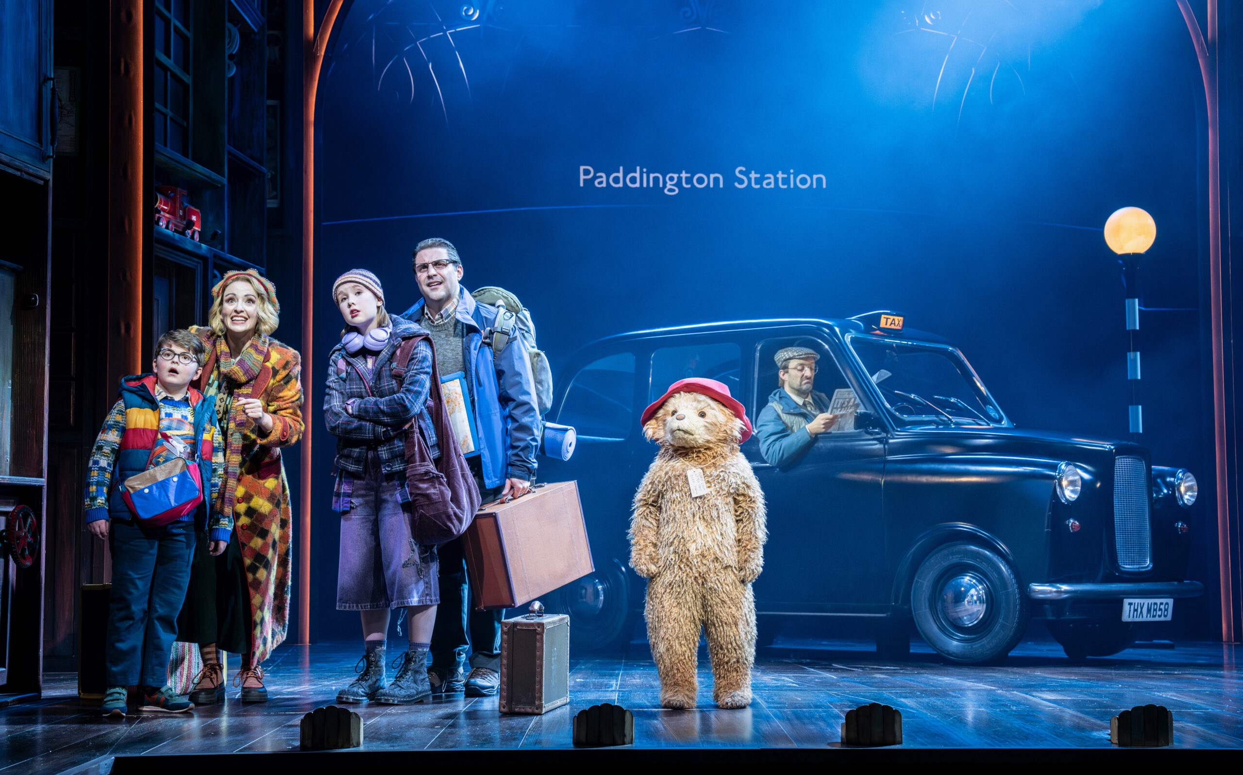 The cast of Paddington the Musical in front of a taxi